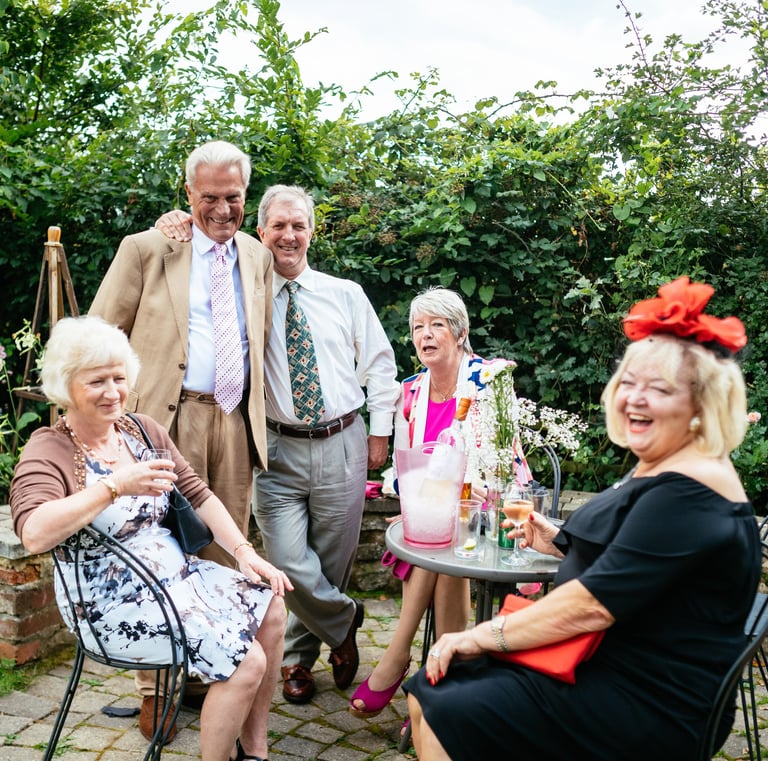 Elegant elderly guests smiling and enjoying drinks at an outdoor wedding party celebration.