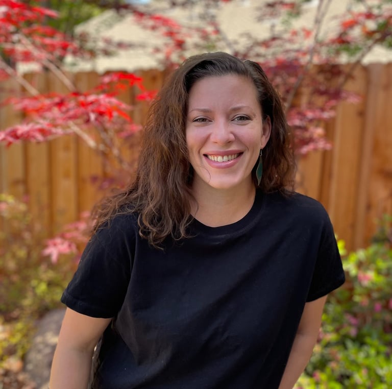 female author in a black shirt and jeans standing in front of a fence