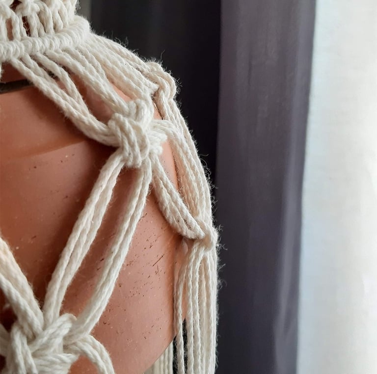 Primer plano de un tejido de macramé blanca que sostiene una lámpara de barro