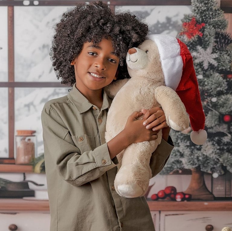 niño de pelo rizado abrazando osito con gorro de Papá Noel