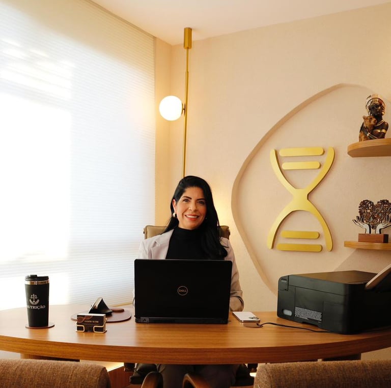 Vanessa Ganime em seu novo consultório sentada na cadeira em uma mesa com o seu laptop.