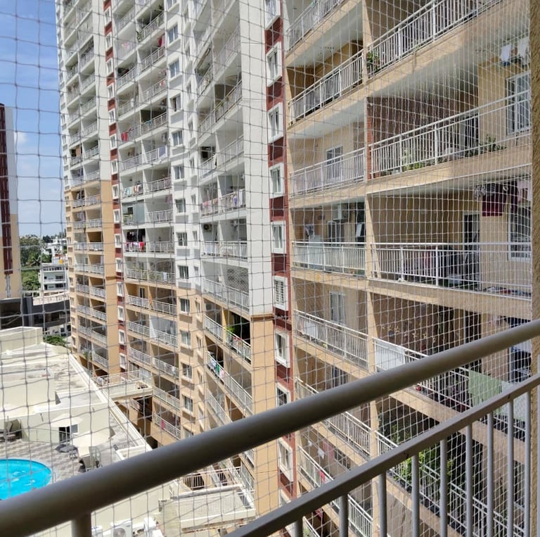A technician carefully installing a sturdy safety net on a high-rise balcony overlooking Sarjapura R