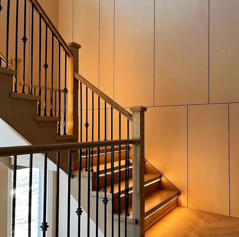 Modern wooden staircase featuring integrated LED tread lighting and black iron balusters.