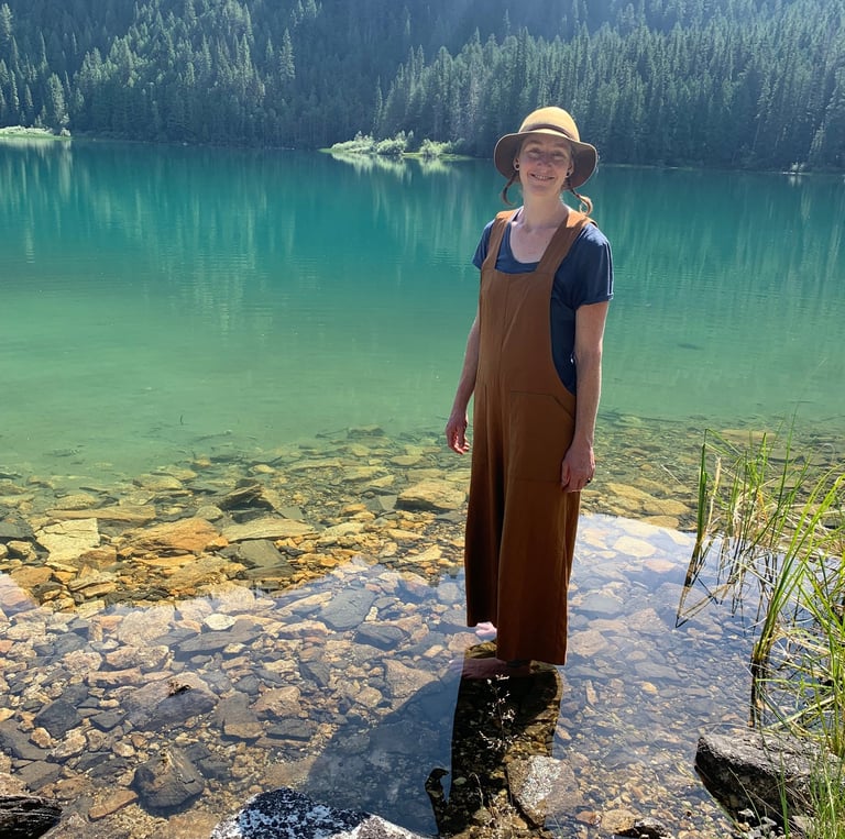 woman with hat standing in green water. rocks visible in water and mountain in background