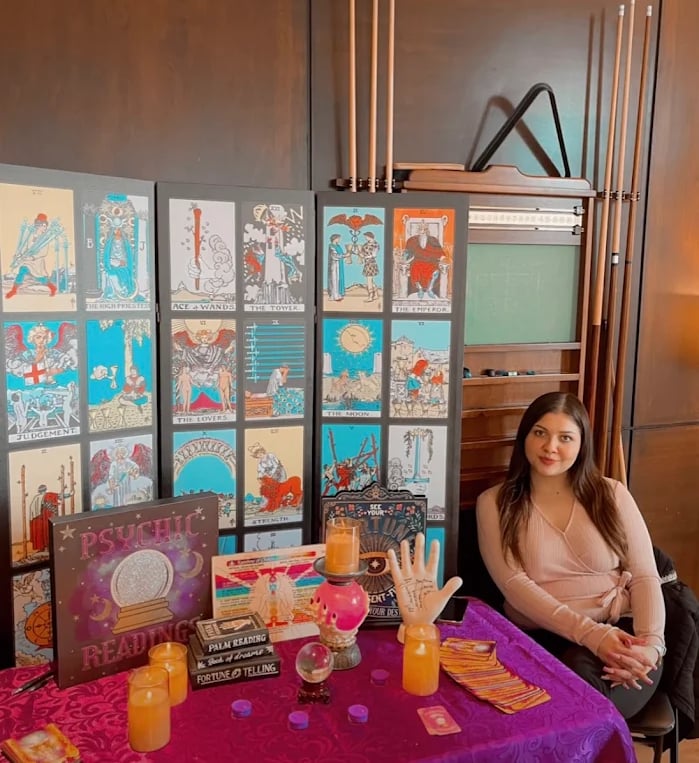 Professional psychic sitting at a fortune telling table with tarot cards, candles, and a palm reading hand.