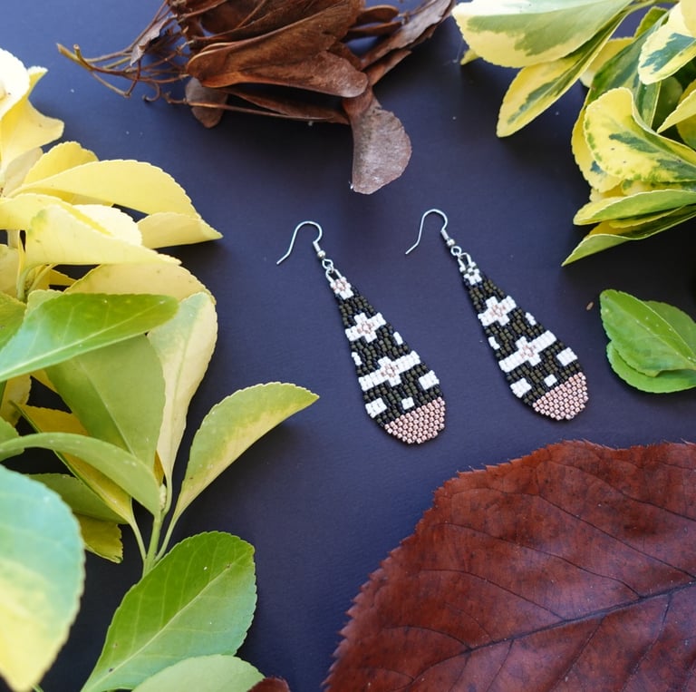 A pair of beaded earrings with to a bunch of leaves and flowers on a table