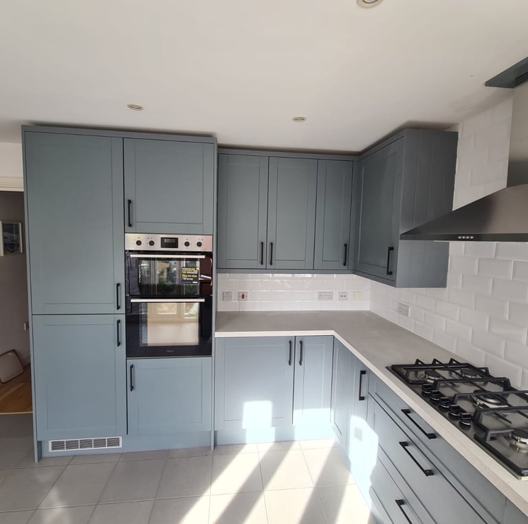 Modern blue kitchen cabinets with white subway tile backsplash, built-in double oven, and gas hob.