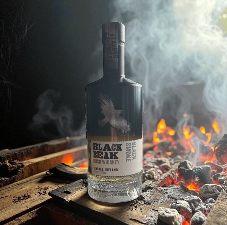 A bottle of Black Beak Black Smoke Irish Whiskey sits on wood planks next to a smoky charcoal fire.