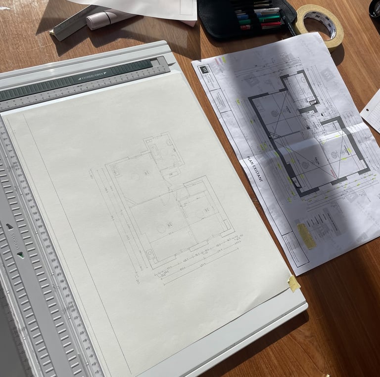 Architectural floor plan sketches and blueprints on a wooden desk with a drafting board and tools.