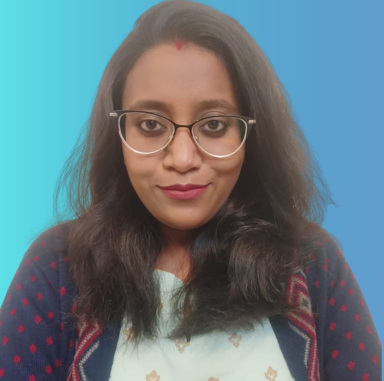 Professional portrait of an Indian woman wearing glasses and a patterned sweater against a blue background.