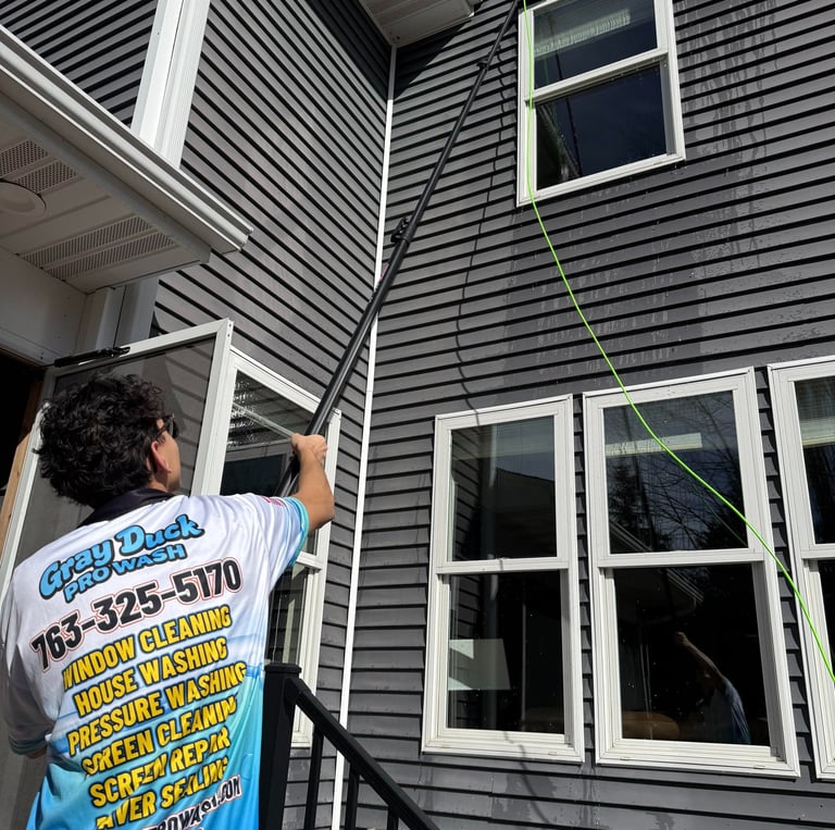 Gray Duck Pro Wash employee cleaning windows on a two-story home using a water-fed system.