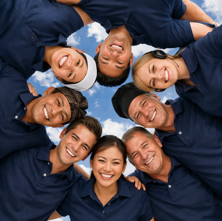 Diverse team of smiling coworkers in blue uniforms huddling in a circle under a blue sky.