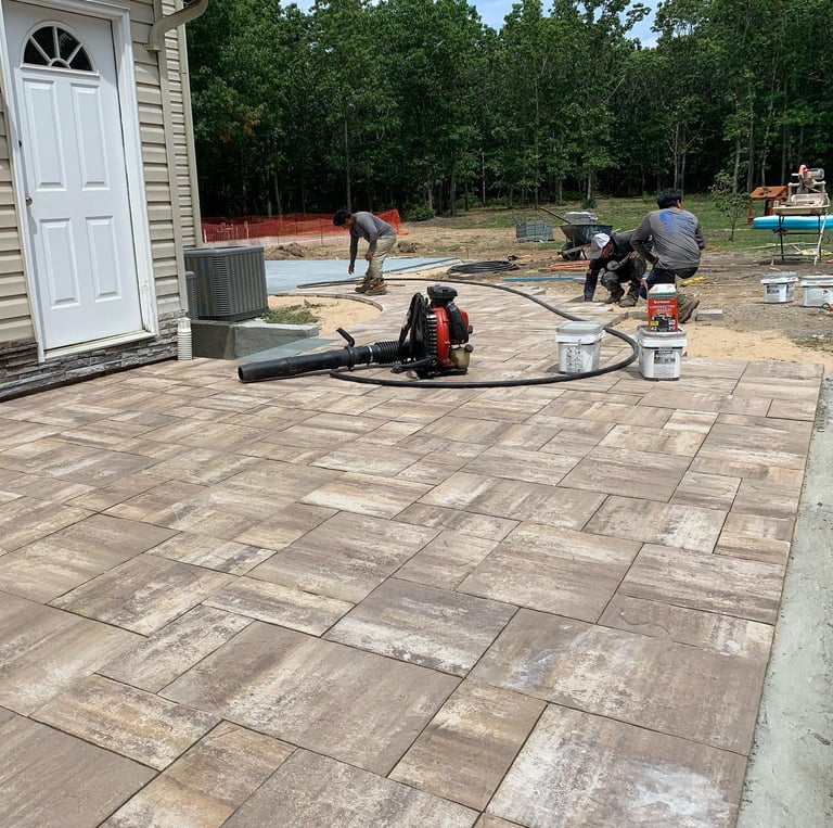 Custom paver patio installation in Port Jefferson Station backyard with outdoor furniture and landsc