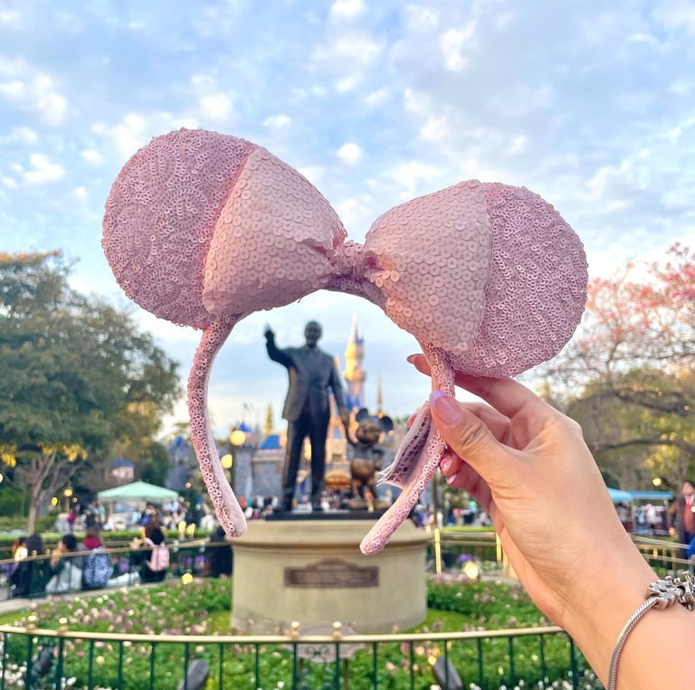 Mano sosteniendo orejitas de Minnie Mouse frente al castillo de Disneyland