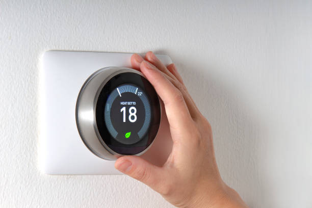 Hand adjusting a smart digital thermostat on a white wall to save energy.