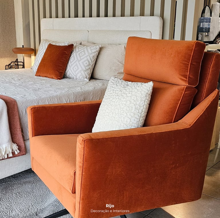 Poltrona moderna de veludo laranja com uma almofada branca num quarto com decoração elegante.