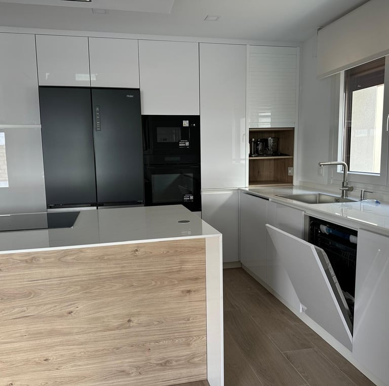 Cocina blanca y madera, isla central, electrodomésticos negros integrados.