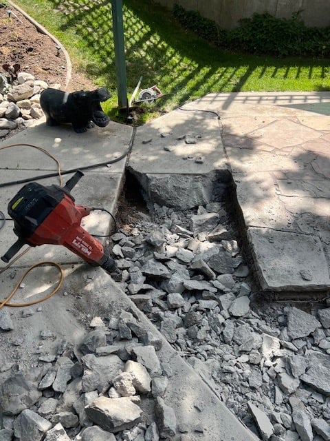 A red jack hammer in a pit of broken up concrete