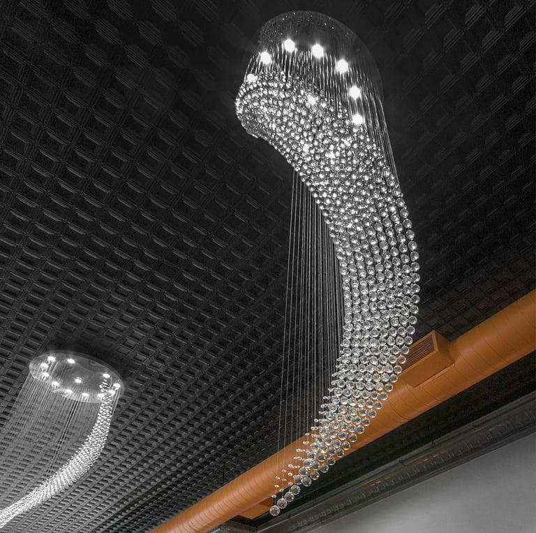 Modern cascading crystal raindrop chandelier lighting hanging from a dark coffered ceiling.