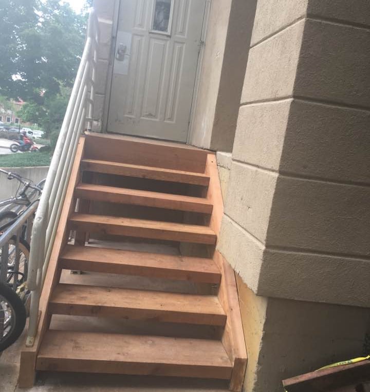 a finished wooden staircase  leading to a door with metal handrail on left side