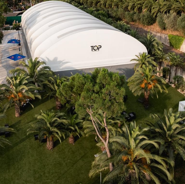 Aerial view of a large white event tent and lounge area surrounded by lush palm trees.