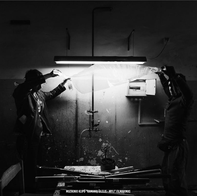 Du filmavimo komandos nariai montuoja apšvietimo įrangą nespalvoto muzikinio vaizdo klipo gamybai.