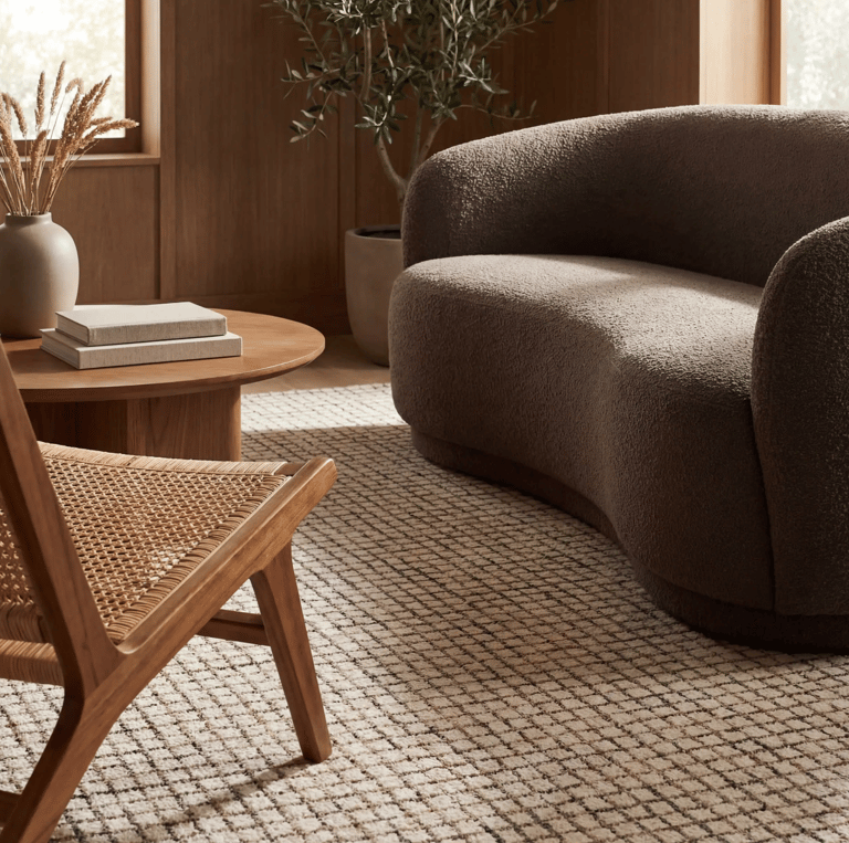 Modern living room with a brown boucle loveseat, woven rattan chair, and neutral grid area rug.