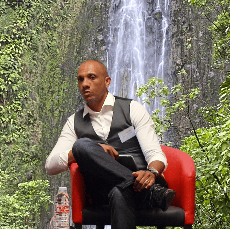 Bruno Valery lors d’une conférence sur le tourisme en Guadeloupe, avec les chutes du Carbet en arrière-plan.