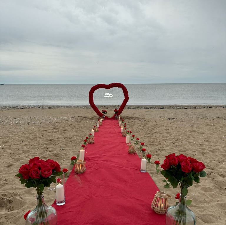 demande en mariage sur la plage avec une arche en forme de coeur orné de fleurs et d'un tapis rouge