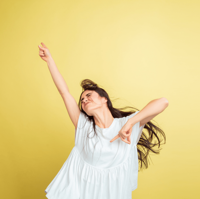 L'immagine mostra una donna che indossa una blusa bianca, posando con un'espressione energica e gioiosa su uno sfondo giallo.