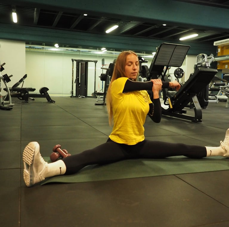 Una donna in maglia gialla esegue uno stretching in spaccata seduta, allungando il braccio per un esercizio di mobilità,