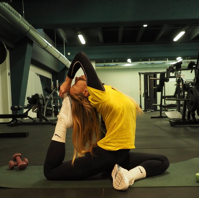 Una donna indossa una maglietta gialla con leggings neri e calze bianche mentre esegue una complessa posa yoga su un tappetin
