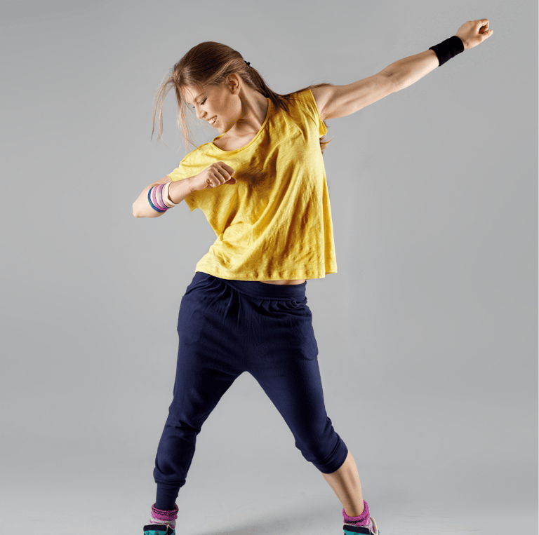 Una donna che danza con energia, indossando una maglietta gialla, pantaloni blu scuro e scarpe sportive nere con dettagli tur