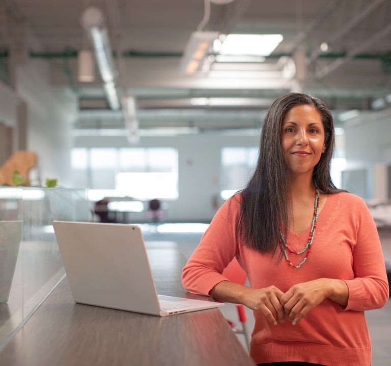 Professionelle Frau in einem modernen Büro, die an einem Stehtisch neben einem Laptop steht.