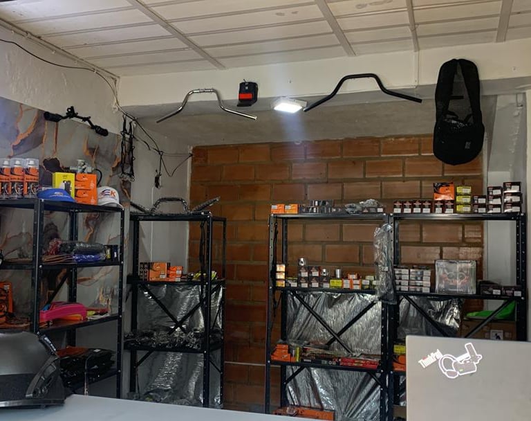 Repuestos y accesorios para motocicletas exhibidos en estanterías metálicas dentro de un taller