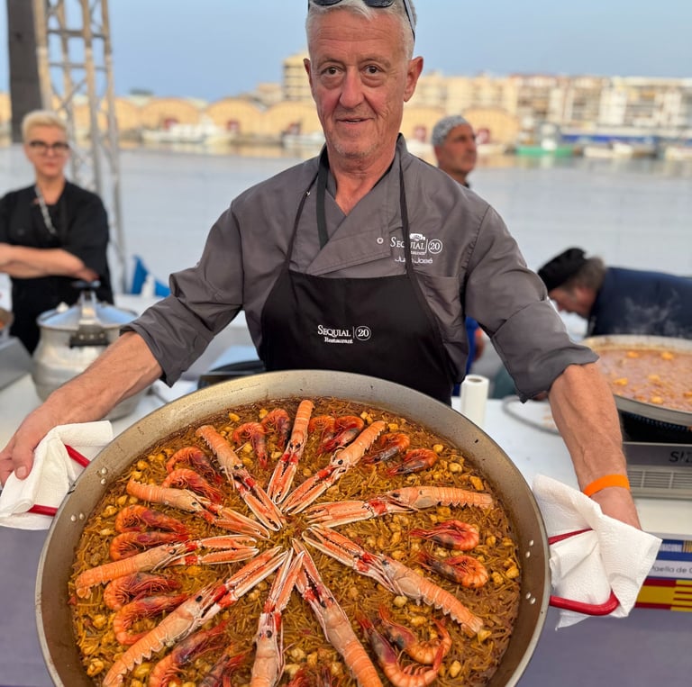 A chef presenting a large authentic Spanish seafood paella with langoustines and shrimp in a traditional pan.