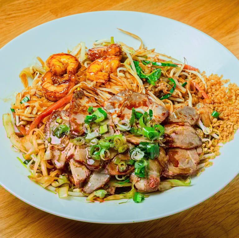 Hu tieu noodles with sliced pork and shrimp, bean sprouts and herbs, served on a white plate