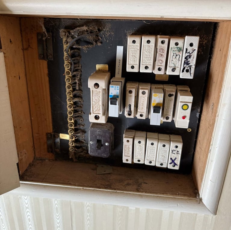 Old electrical switchboard with ceramic fuses and circuit breakers in a recessed wall niche.