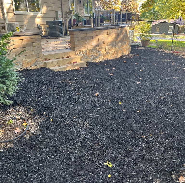 Residential backyard featuring a stone retaining wall and patio surrounded by fresh black mulch.