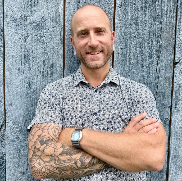 Harrison Blum leaning against gray wooden wall with arms crossed and smiling