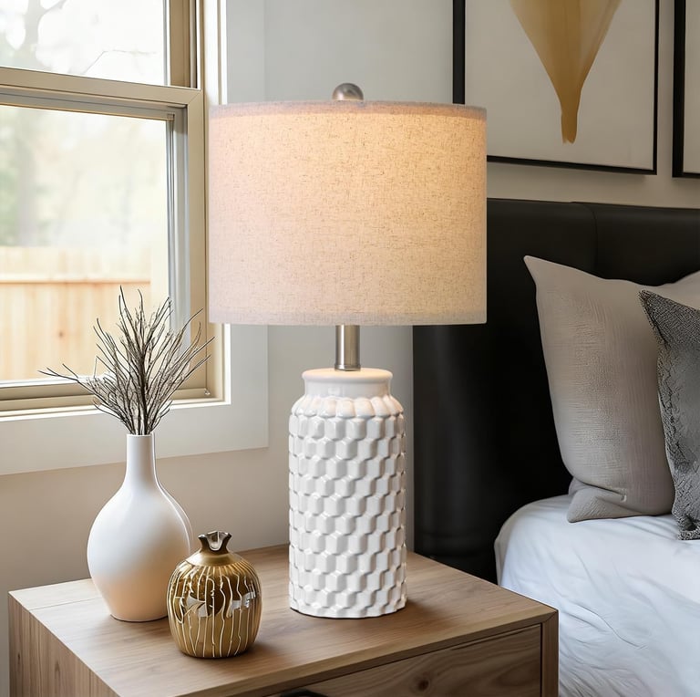 White textured ceramic table lamp with linen shade on a wooden nightstand in a modern bedroom.