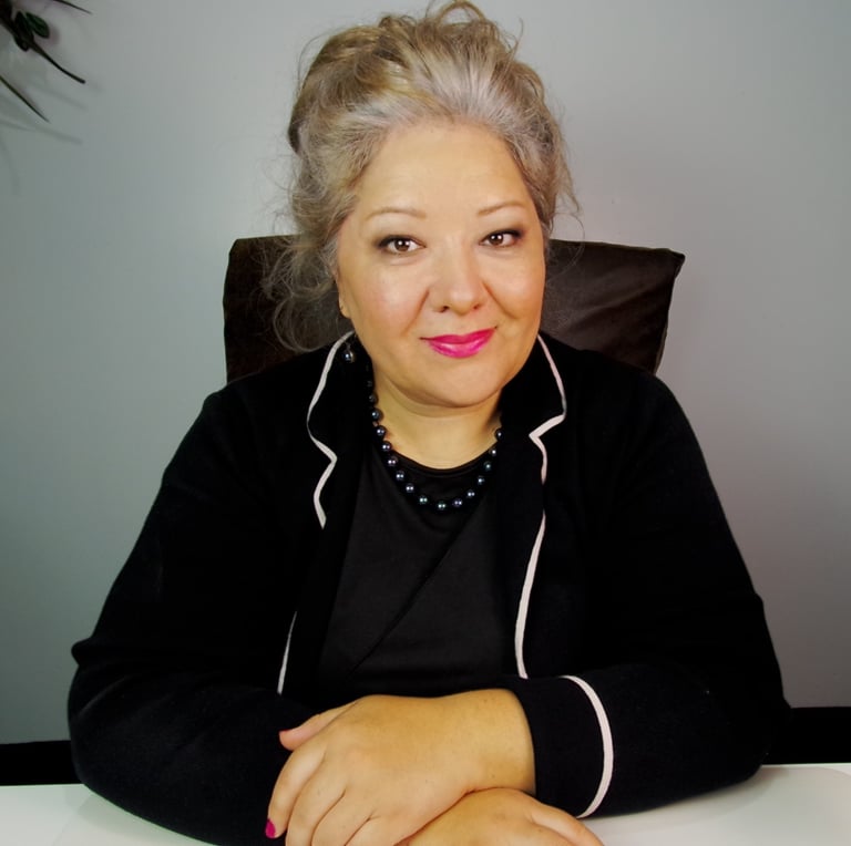 Professional businesswoman with grey hair in a black blazer smiling at an office desk.