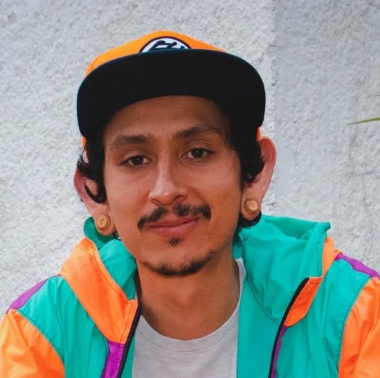 Joven con dilataciones en las orejas, usando una gorra naranja de béisbol y una chaqueta vintage 