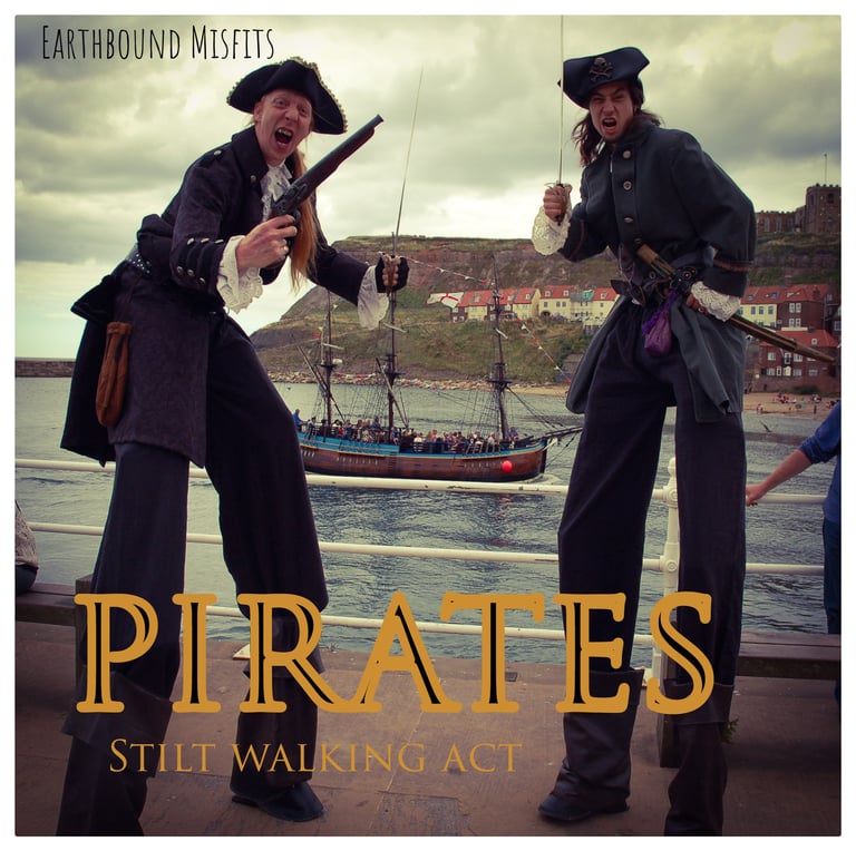 Two Earthbound Misfits performers in pirate costumes on stilts posing by a harbor with a pirate ship.