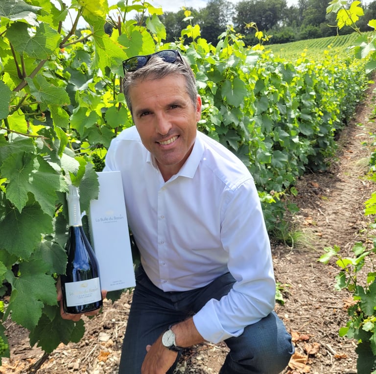Patrice agenouillé dans les vignes tenant une bouteille de Champagne La Bulle du Bassin et son étui 
