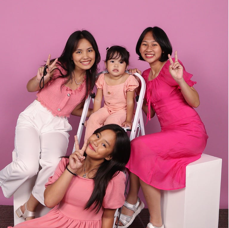 Three young ladies and a small girl in pink dresses on pink background