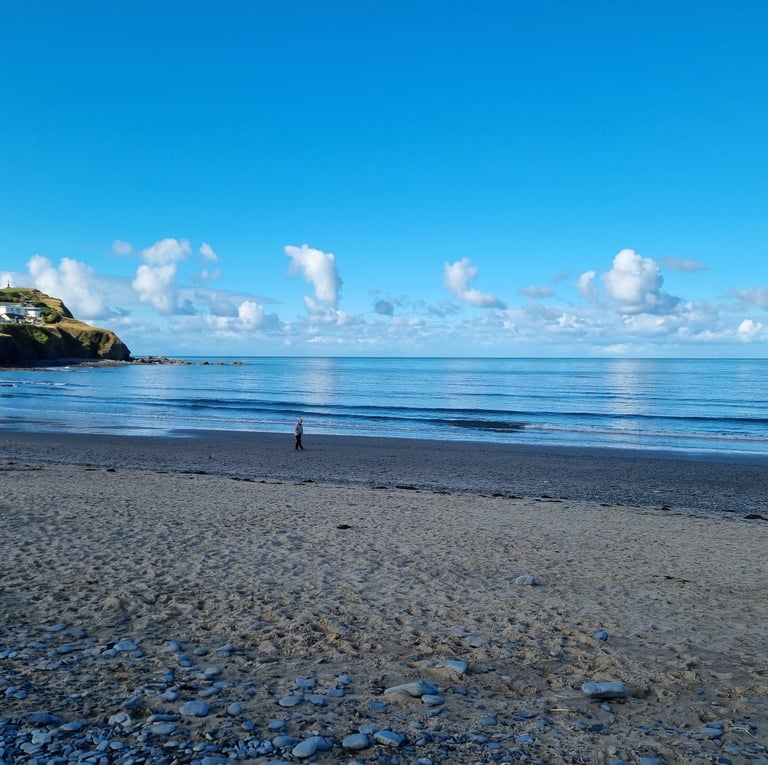 Early morning beach and Borth headland with small waves and smooth clam blue sea and sky