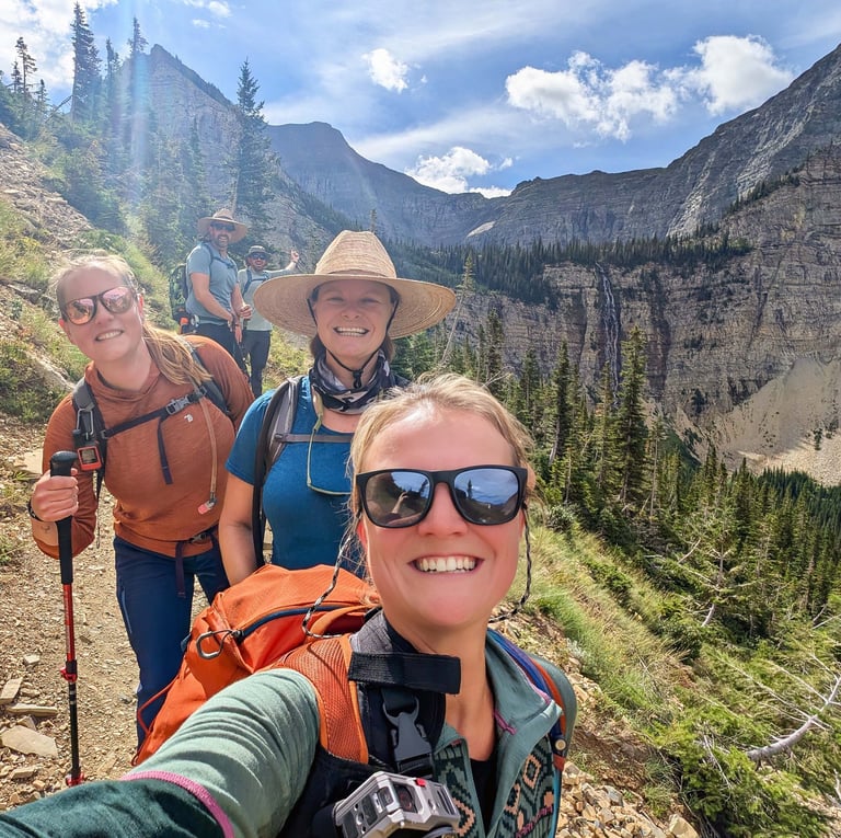 Hikers smiling on the Crypt Lake Trail with Crypt Falls visible in the background in Waterton Lakes