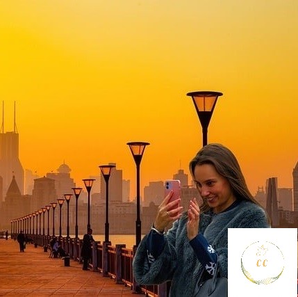 photographie corrigée, femme souriante regardant son portable sur un fond de lumière dorée et sur un bord de fleuve calme