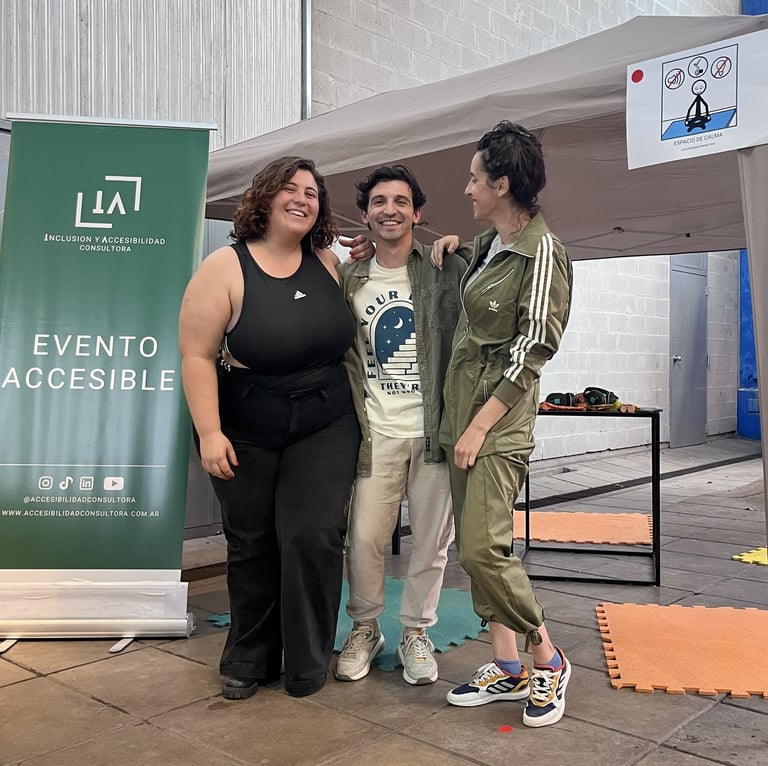 Los integrantes de IA sonríen frente a carpa rotulada “Espacio de calma” en un evento accesible.